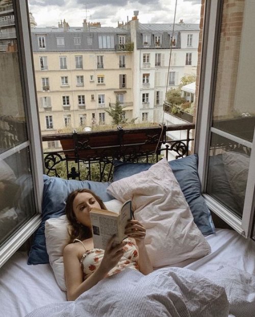 Девушка читает лежа на подоконнике с открытым окном, укрывшись одеялом