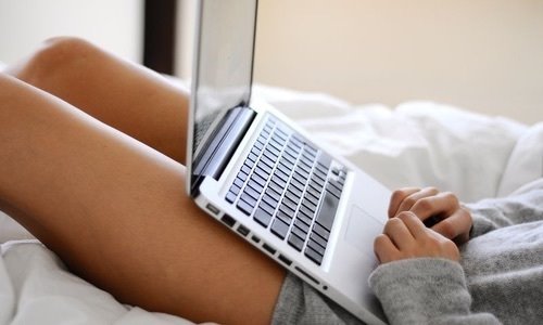 Девушка лежа на кровати дома работает на ноутбуке