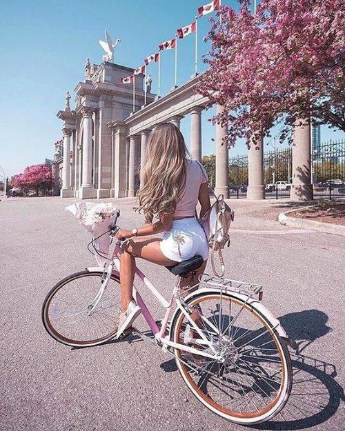 Девушка со спины в коротких белых шортах прикрепила к велосипеду букет цветов