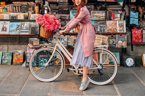 Девушка на книжном рынке с велосипедом и корзиной красных цветов