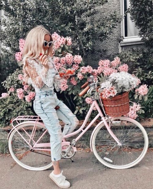 Блондинка с клубникой на велосипеде среди розовых цветов
