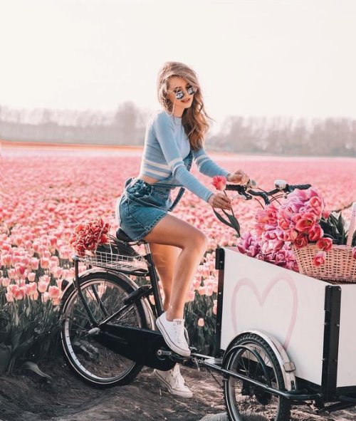 Девушка среди поля с тюльпанами в комбинезоне на цветочном велосипеде
