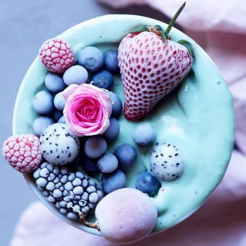 Смузи голубого цвета украшенное замороженными ягодами и розой