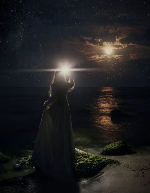Девушка на берегу моря светит луне спиной в платье