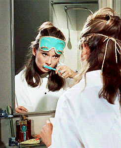 Девушка в маске для сна чистит зубы перед зеркалом