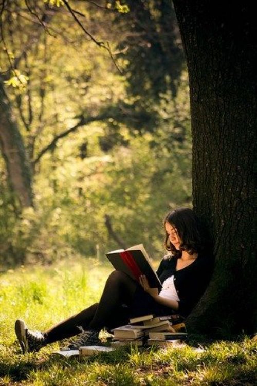 Брюнетка с книгами учится под деревом
