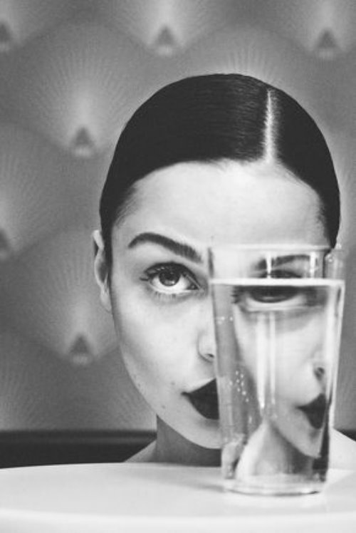 Девушка с прямым пробором волос смотрит вверх рядом с стаканом