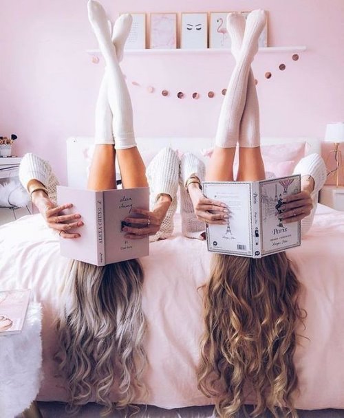 Две девушки в чулочках подняли вверх ноги лежа на кровати в уютной красивой комнате прикрывшись книгами