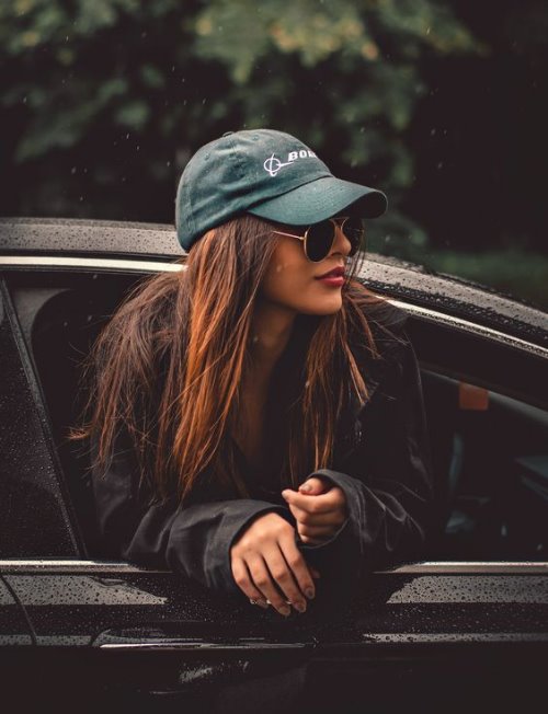 Девушка модельной внешности в кепке высунулась в окно машины под дождем