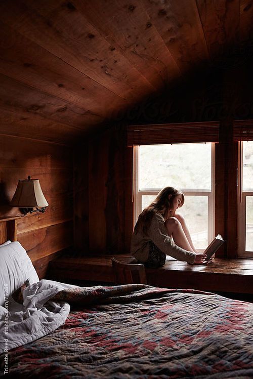 Девушка в деревянном доме на подоконнике читает книгу