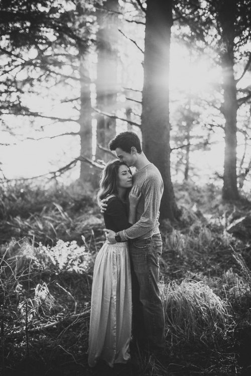Мужчина целует женщину в висок под деревом в лесу