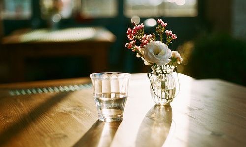 Солнце светит в стакан воды и минивазу на столе в кафе