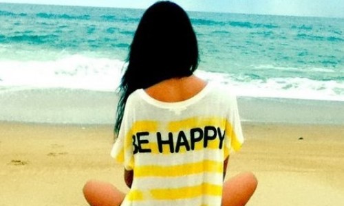 брюнетка в полосатой футболке be happy со спины сидит на пляже
