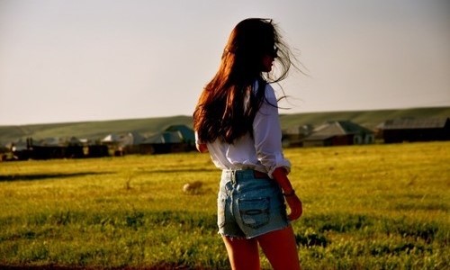 шатенка спиной в белой рубашке и коротких джинсовых шортах на зеленом поле