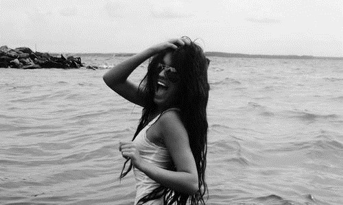 чернобелое фото девушки с длинным темным волосом в солнечных очках которая зашла в холодную морскую воду