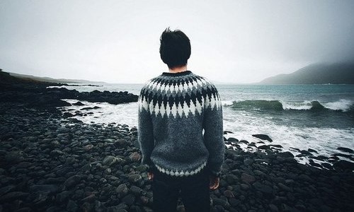 парень спиной на каменном берегу в свитере